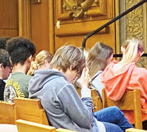 Students wait for assembly speakers while checking notifications and watching videos.  