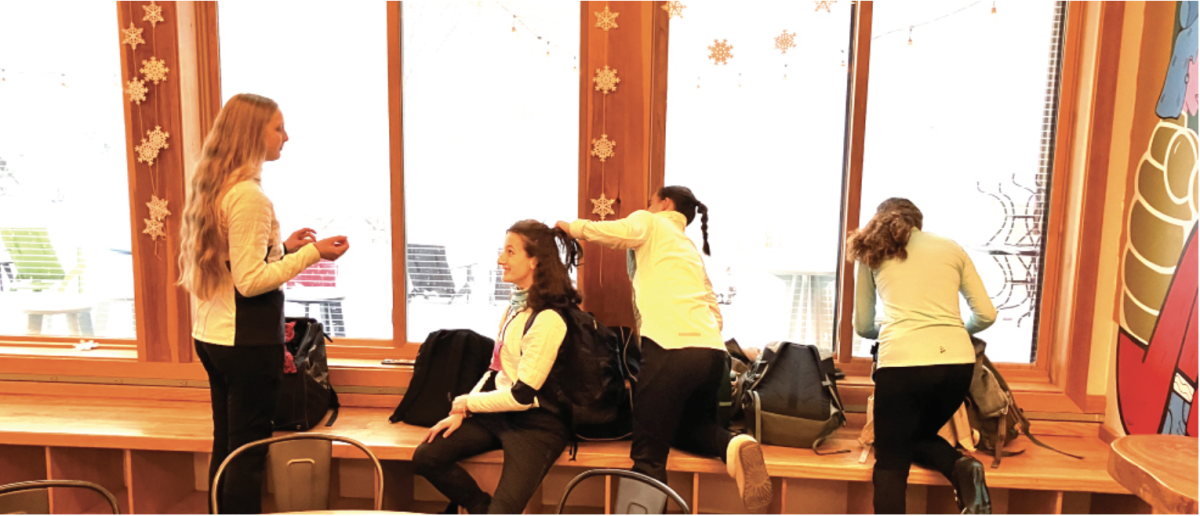 Team members braid each other’s hair and chat as they prepare inside The Trailhead for the cold.